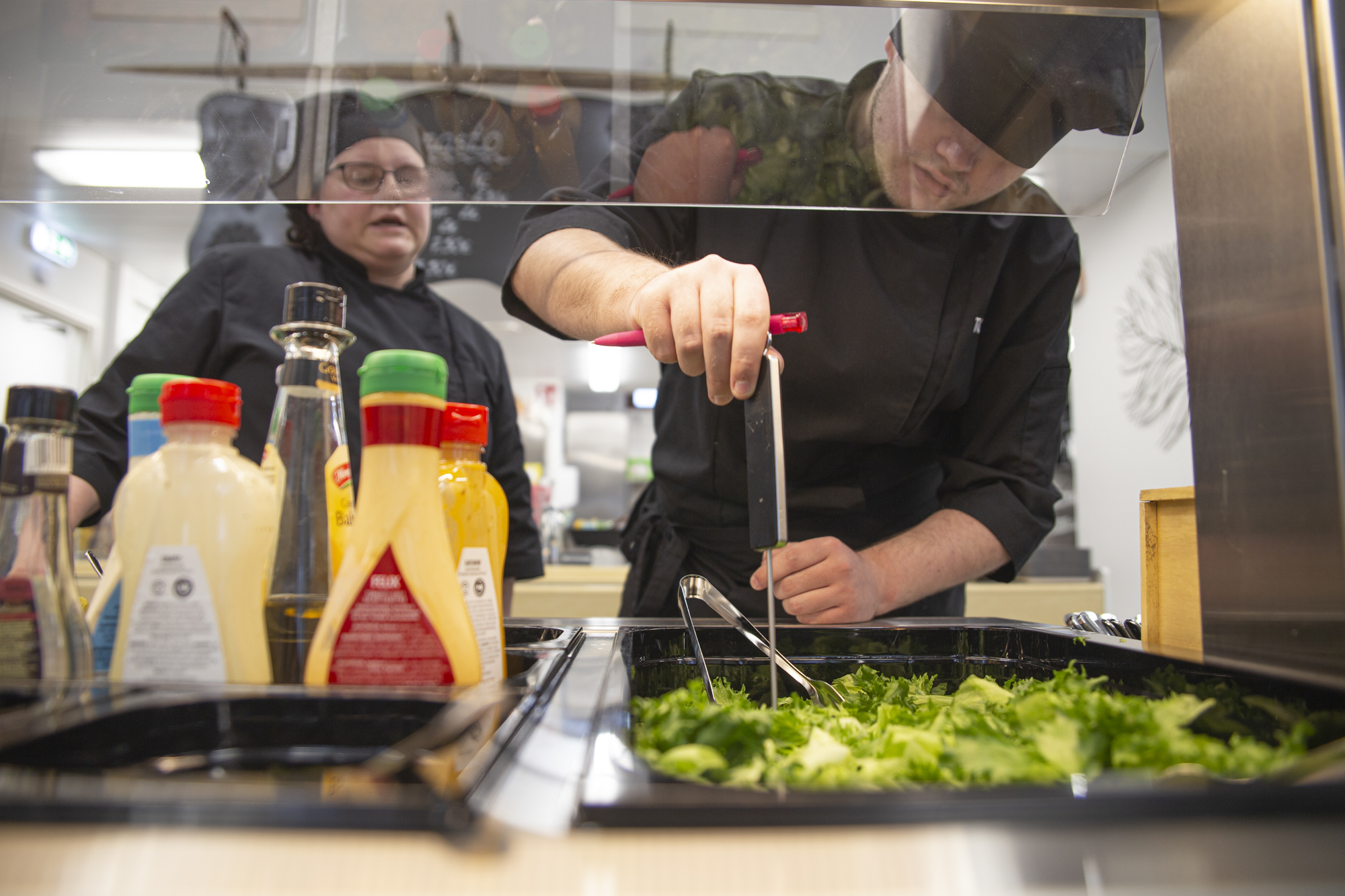 Kokkiopiskelija ottaa lämpötilanäytettä salaattipöydästä.