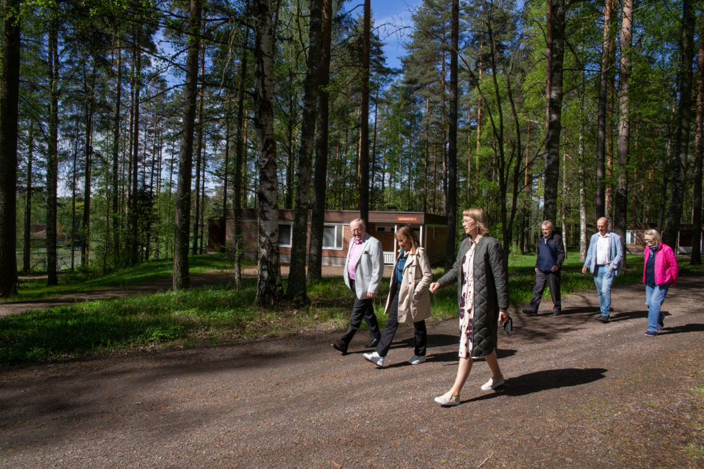 Ryhmä ihmisiä kävelee aurinkoisella metsätiellä.