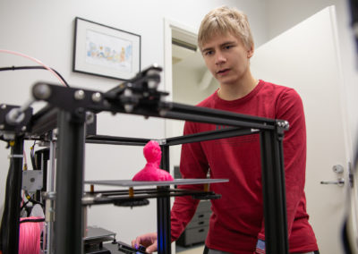 Opiskelija katsoo, kun 3D-tulostin tulostaa muovipäätä.
