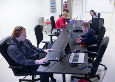 Opiskelijoita pitkän työpöydän äärellä kannettavien tietokoneiden kanssa.