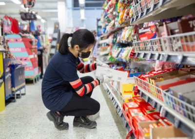 Merkonomiopiskelija hyllyttää karkkipatukoita supermarketin karkkiosastolla.