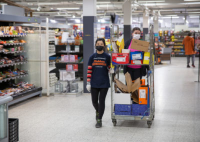 Merkonomiopiskelijat kuljettavat pakkauspahveja rullakossa supermarketissa.