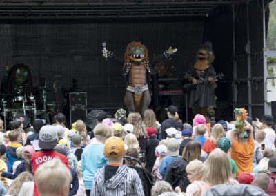 Hevisaurus-bändi esiintyy puistolavalla suurelle lapsiyleisölle.