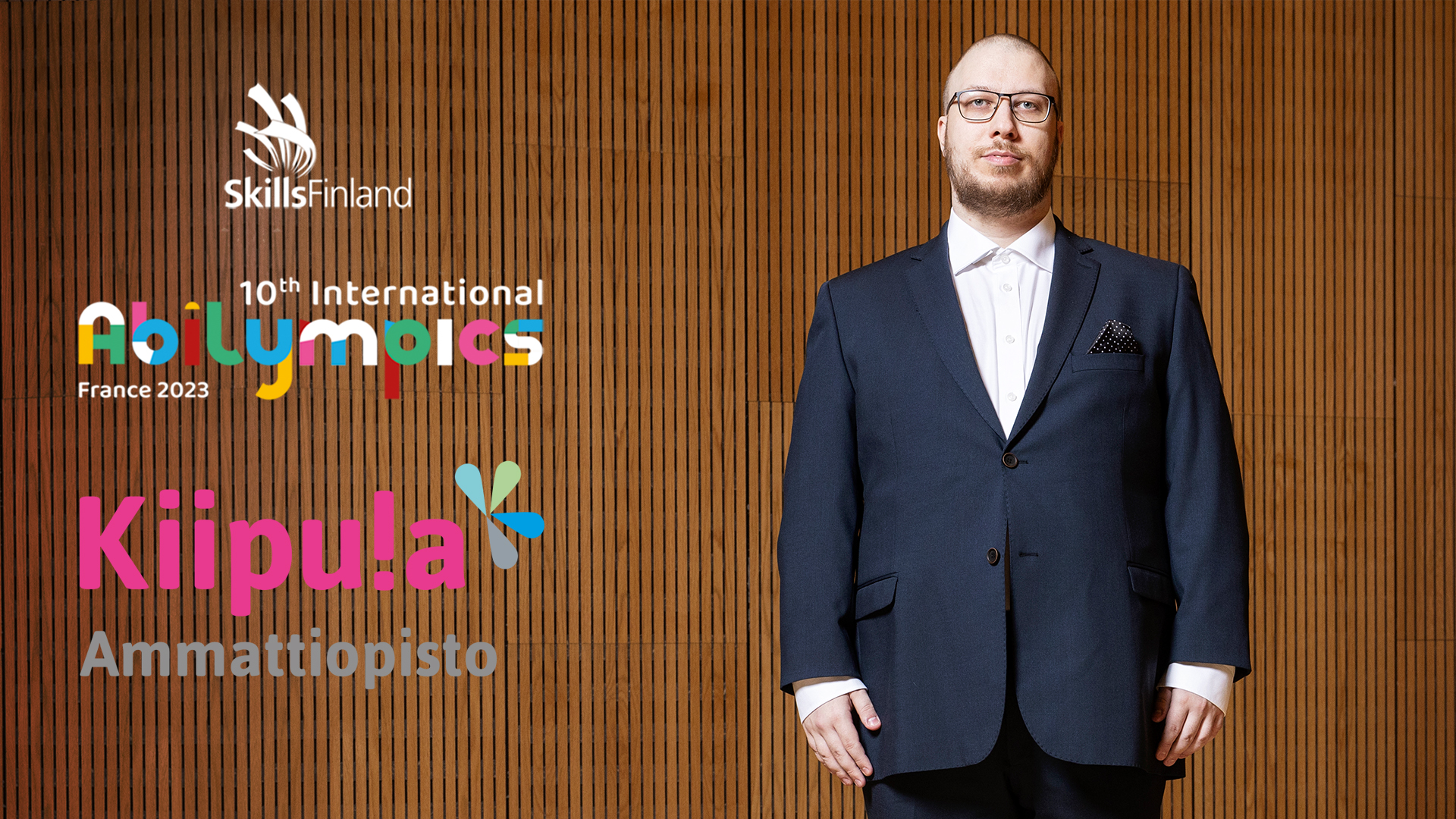 Jani Jalassalo seisoo puku päällä. Kuvassa myös Skills Finland ry:n, Abilympicsin sekä Kiipulan ammattiopiston logot.