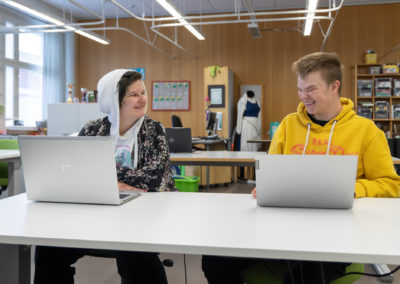 Kaksi opiskelijaa luokkatilassa kannettavien tietokoneiden äärellä.