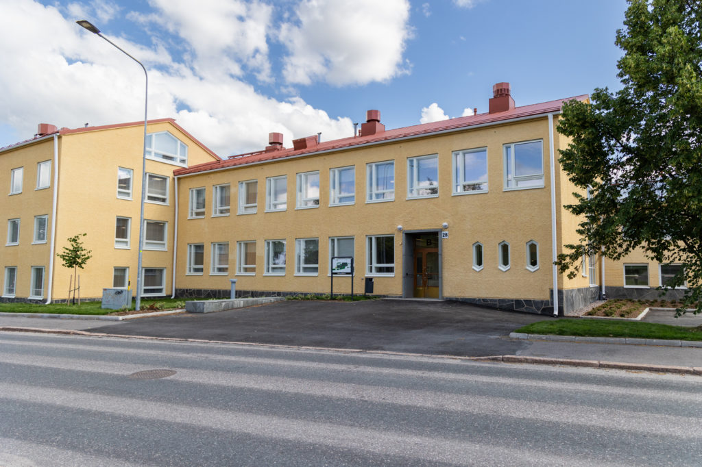 Vaaleankeltaiseksi rapattu koulurakennus, jossa on punainen katto.