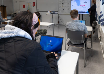 Opiskelijat istuvat luokassa kannettavien tietokoneiden äärellä. Katsovat yhdessä uutisia televisiosta.