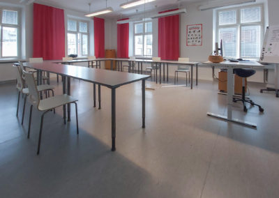 Valoisassa luokkatilassa pöydät U-muodostelmassa. Opettajan pöytä edessä.