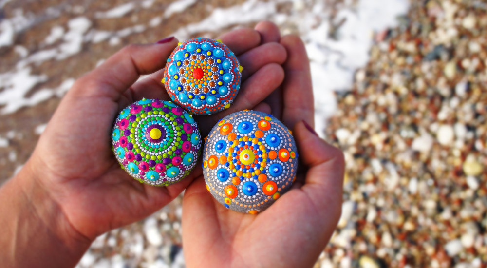 Kädet joissa on kolme värikkäästi maalattua kiveä.